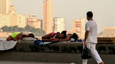 Un homme passe devant des femmes qui dorment sur le Malecon à La Havane lors d'une coupure de courant nationale, le 3 août 2026