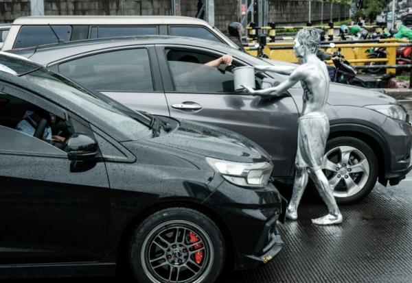 L'artiste de rue Ari Munandar (d), le corps recouvert de peinture argentée, fait la manche sous la pluie à un carrefour de Jakarta, le 1er avril 2025 en Indonésie