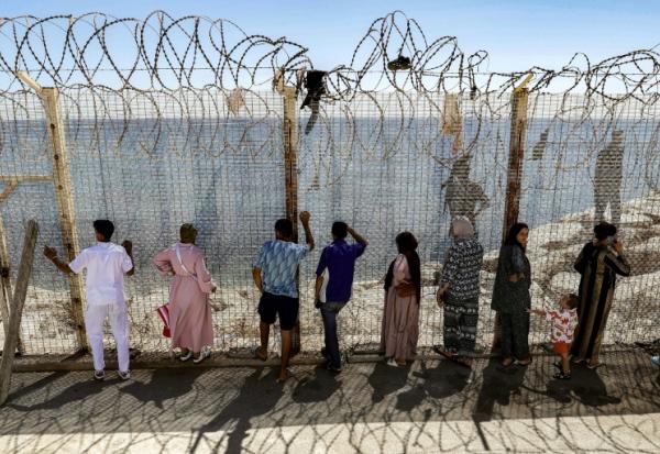 Des personnes attendent derrière une clôture surmontée de barbelés le retour de proches ayant tenté de franchir la frontière pour entrer dans l’enclave espagnole de Ceuta, le 2 août 2026 à Fnideq