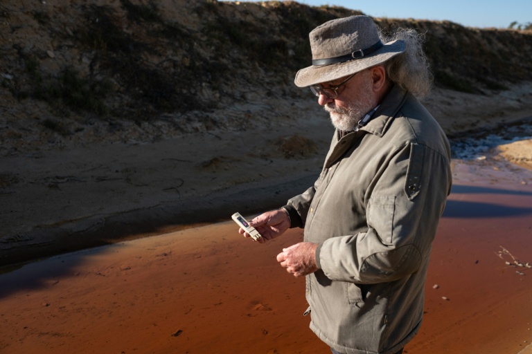 David van Wyk, chercheur principal à la Bench Marks Foundation, effectue des tests dans un cours d'eau à la décharge de la mine de Snake Park, à Soweto, le 30 mai 2025 en Afrique du Sud
