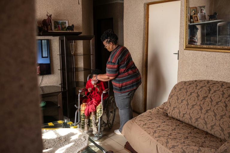 Lilly Stebe donne de l'eau à sa fille adoptive, Okuhle, née avec une paralysie cérébrale, dans leur maison de Snake Park, à Soweto, le 23 mai 2025 en Afrique du Sud