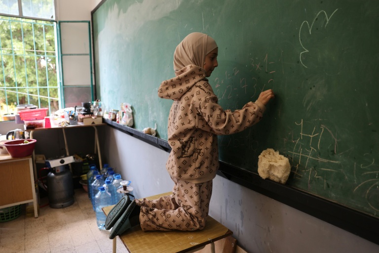 Une jeune fille effectue des calculs arithmétiques sur un tableau dans une salle de classe d'une école publique transformée en refuge pour personnes déplacées à Dekwaneh, au nord de Beyrouth, le 24 mars 2026 au Liban