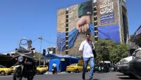 Des passants traversent une rue devant un panneau d'affichage apposé sur la façade d'un immeuble représentant le détroit d'Ormuz, avec une légende en persan indiquant "Pour toujours entre les mains de l'Iran", à Téhéran, le 25 mai 2026