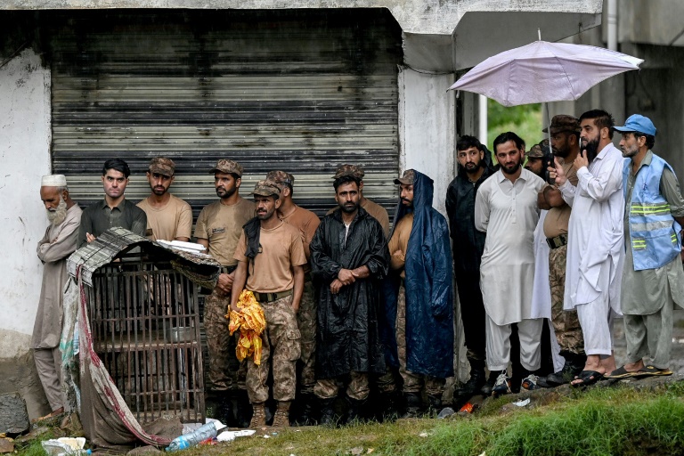 Des sauveteurs et du personnel militaire s'abritent de la pluie sous le toit d'un bâtiment alors que le niveau des eaux de crue monte dans le district de Buner, dans la province de Khyber Pakhtunkhwa, le 18 août 2025 au Pakistan