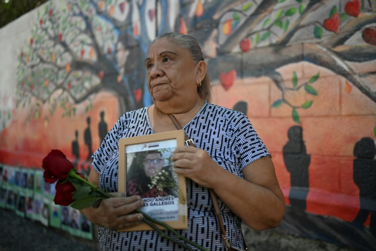Sandra Gallegos tient un portrait de son fils disparu, Fernando Rosales, lors de l'inauguration d'une fresque murale en hommage aux personnes disparues, à l'Université d'El Salvador, à San Salvador, le 19 mars 2026