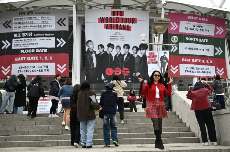 Des fans posent pour des photos devant une grande banderole à l'effigie du boys band de K-pop BTS, sur les marches menant au stade où le groupe se produira, à Goyang, le 9 avril 2026
