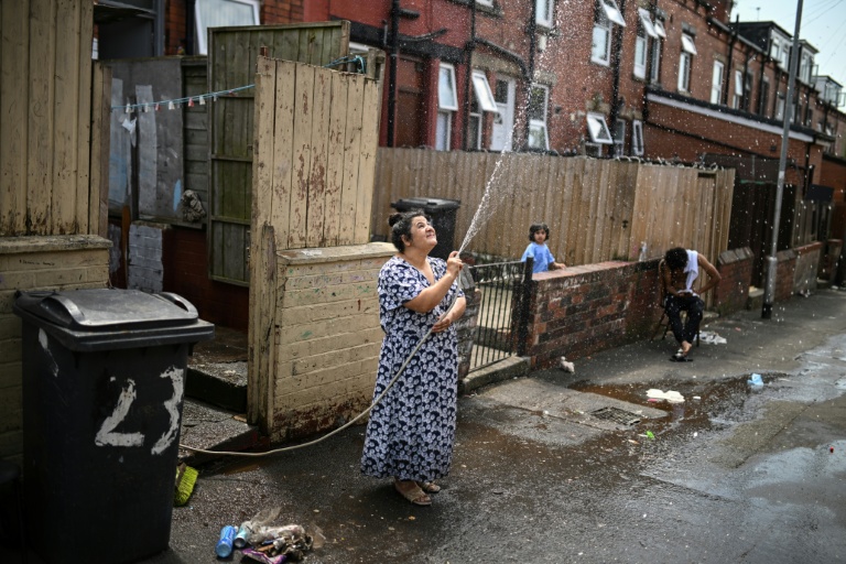 Une femme asperge une allée devant chez elle pour rafraichir à Leeds en Angleterre le 25 juin 2026