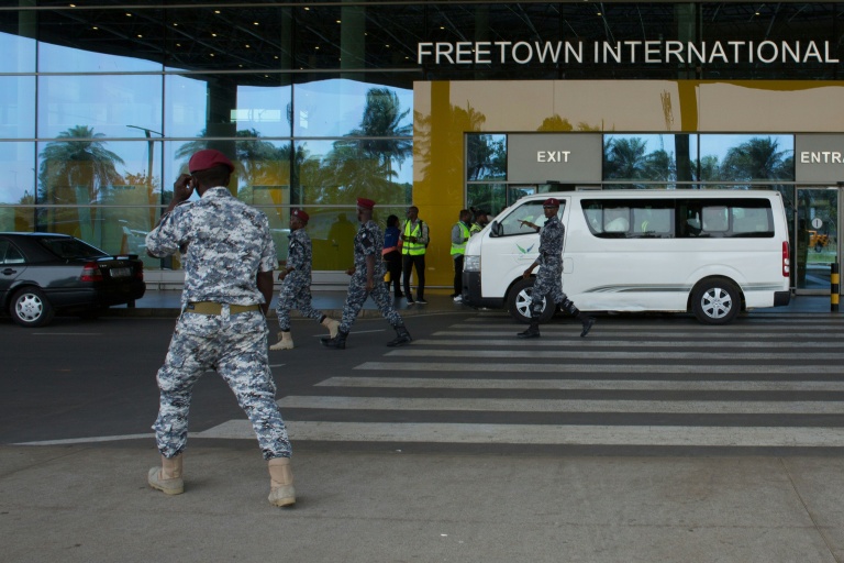 Des agents de sécurité escortent des migrants vers un centre de l'Agence nationale de santé publique (NPHA) après leur arrivée à l'aéroport international de Freetown, le 20 mai 2026 à Lungi, en Sierra Leone