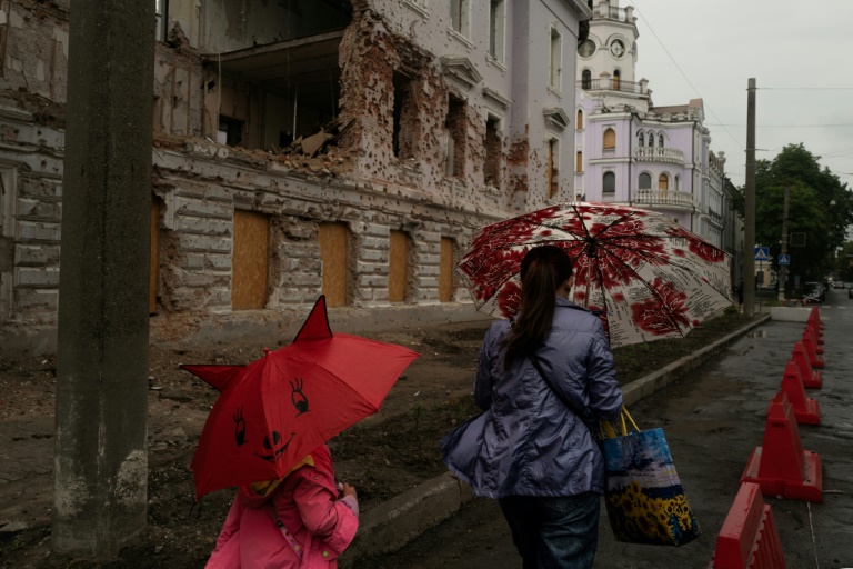 Une mère et sa fille passent près d'un bâtiment détruit par un bombardement russe, le 12 juin 2025 à Soumy, dans le nord-est de l'Ukraine