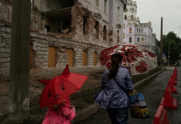 Une mère et sa fille passent près d'un bâtiment détruit par un bombardement russe, le 12 juin 2025 à Soumy, dans le nord-est de l'Ukraine 
