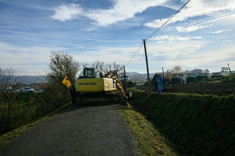 Un agriculteur, à l'aide d'un tracteur, bloque la route avec des troncs d'arbres lors d'une manifestation pour empêcher l'abattage d'un troupeau de 200 vaches, à la suite de la détection de la dermatose nodulaire contagieuse (DNC) aux Bordes-sur-Arize, le 11 décembre 2025 en Ariège