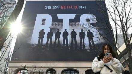 Une femme consulte son smartphone devant un panneau d'affichage annonçant le concert de retour du groupe de K-pop BTS, le 17 mars 2026 à Séoul