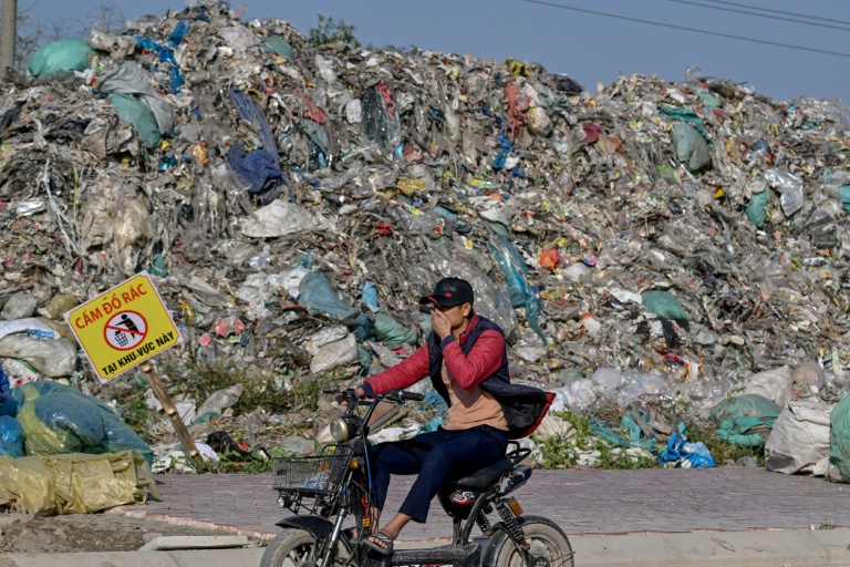 Un homme passe en deux-roues devant une montagne de déchets, en périphérie de Hanoï, le 25 novembre 2025