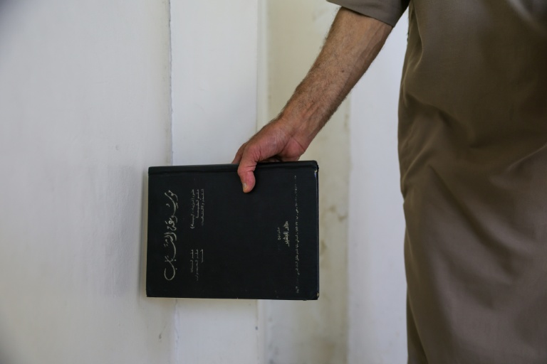 Mustafa Khaled Alwan tient un livre près de l'emplacement du faux mur qui dissimulait sa bibliothèque, chez lui à Homs, en Syrie, le 19 septembre 2026
