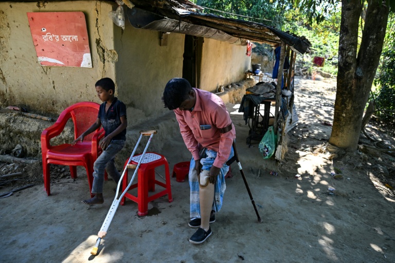 Ali Hossain (à droite), un Bangladais de 40 ans qui a perdu une jambe à cause d’une mine lorsqu'il ramassait du bois, retire sa prothèse devant sa maison dans le district de Bandarban le 19 décembre 2025