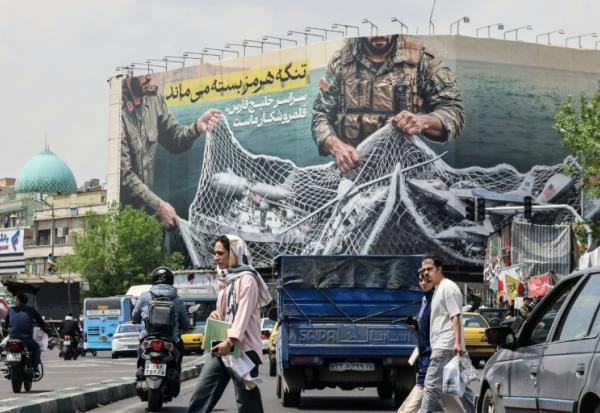 Des Iraniens passent devant un panneau d'affichage géant indiquant "Le détroit d'Ormuz reste fermé" sur la place de la Révolution à Téhéran, le 22 avril 2026