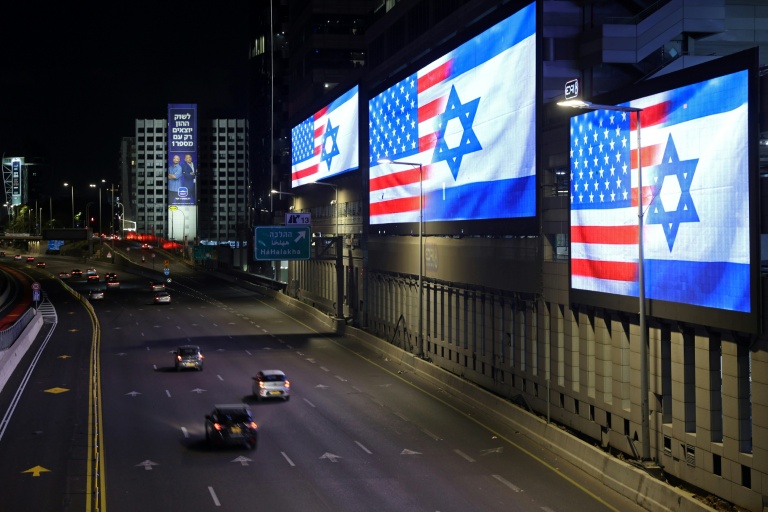 Des voitures passent le 4 mars 2026 devant des écrans géants installés le long de l'autoroute à Tel Aviv, affichant les drapeaux des Etats-Unis et d'Israël