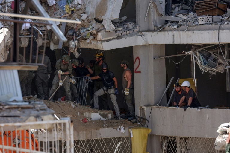 Secouristes et militaires israéliens fouillent les décombres d'un bâtiment lourdement endommagé par des tirs de missiles iraniens dans la ville côtière de Bat Yam, au sud de Tel-Aviv, le 15 juin 2025