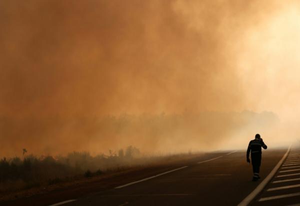 Un pompier marche sur une route à la lisière d'une zone en feu à Ares, le 26 juillet 2026, alors qu'un incendie de forêt ravage la forêt au nord du bassin d'Arcachon (Gironde) depuis le 22 juillet