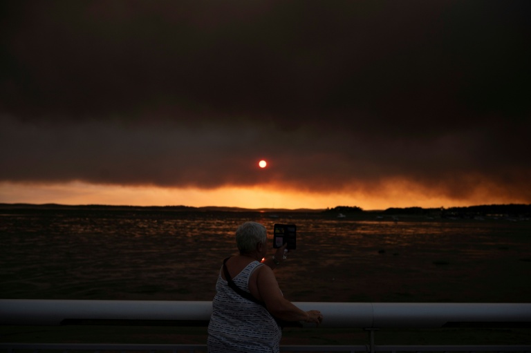 Une femme observe la fumée depuis la plage à Andernos-les-Bains lors d'un incendie dans la forêt de Lège-Cap-Ferret, dans le sud-ouest de la France, le 23 juillet 2026, alors qu'une partie de la zone voisine a été évacuée