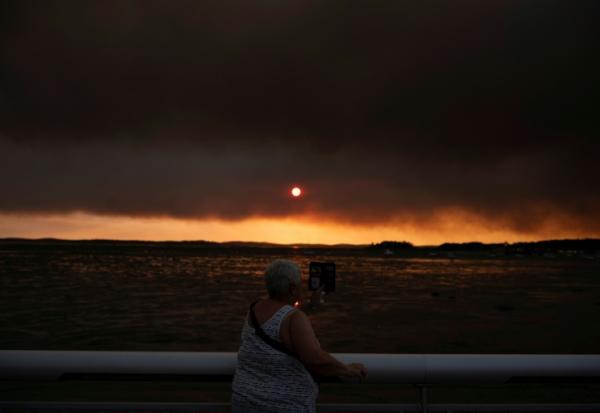 Une femme observe la fumée depuis la plage à Andernos-les-Bains lors d'un incendie dans la forêt de Lège-Cap-Ferret, dans le sud-ouest de la France, le 23 juillet 2026, alors qu'une partie de la zone voisine a été évacuée