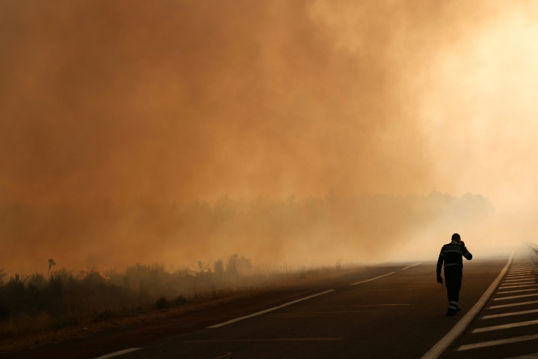 Un pompier marche au bord d'une route, près d'une zone touchée par l'incendie en Gironde, à Arès, le 26 juillet 2026