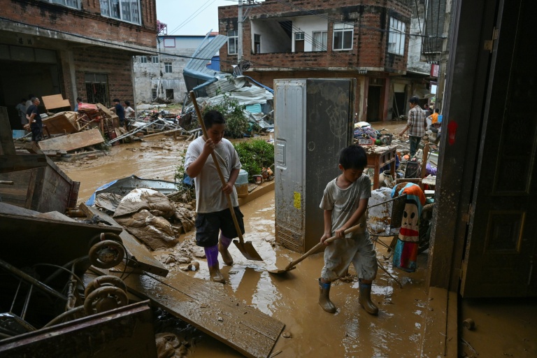 Des enfants aident à nettoyer la boue dans leur maison inondée lorsqu'un réservoir s’est effondré le 6 juillet, dans le village de Liulan, dans la ville de Hengzhou, dans la région du Guangxi, au sud-ouest de la Chine, le 8 juillet 2026