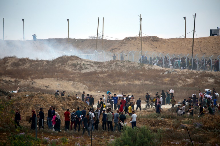 Des Palestiniens déplacés se dirigent vers un centre de distribution d'aide humanitaire, alors que des bombes fumigènes sont tirées par les troupes israéliennes, dans le centre de la bande de Gaza, le 8 juin 2025