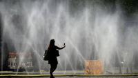 Une femme prend une photo de tuyaux d'arrosage déversant de l'eau pour apporter un peu de fraîcheur face à la chaleur estivale, à Cologne, dans l'ouest de l'Allemagne, le 25 juin 2026