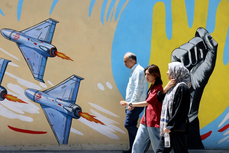 Des Iraniens passent devant des graffitis anti-américains et anti-israéliens, à Téhéran le 10 mai 2026