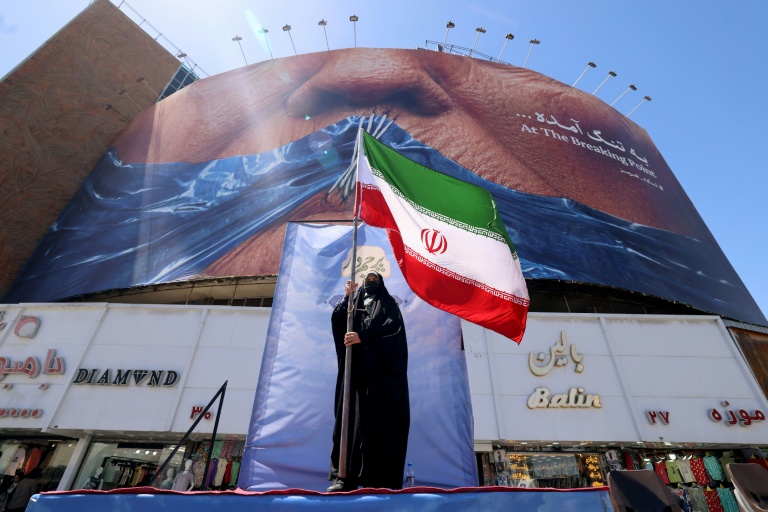 Une Iranienne brandit le drapeau de son pays, devant une panneau représentant le président américain Donald Trump, à Téhéran le 10 mai 2026