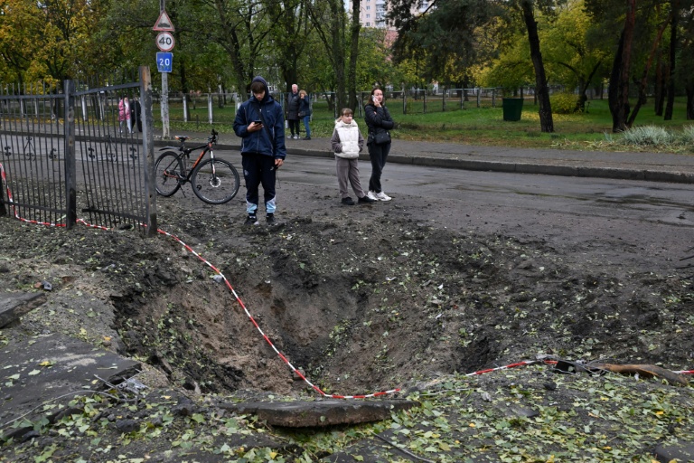 Des personnes se tiennent près d'un cratère causé par un missile, à proximité d'une école endommagée à la suite d'une attaque russe à Kiev, le 19 octobre 2026