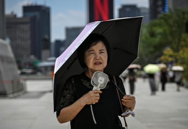 Une femme sous un parapluie avec un ventilateur portatif, le 12 juillet 2026 à Séoul 