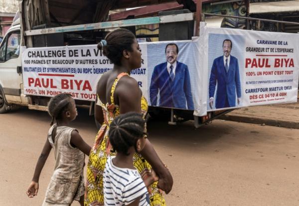 Une femme et ses enfants traversent la rue près d'un camion de campagne du président sortant du Cameroun, Paul Biya, à Yaoundé le 11 octobre 2025