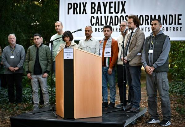 (g-d) Le journaliste de guerre américain Jon Lee Anderson, les collaborateurs de l'AFP Belal Al-Sabbagh, Mohannad Shahwan, Mai Yaghi, Adel Zaanoun, Said Khatib, Mohammed Abed, le directeur général de RSF Thibault Bruttin et le collaborateur de l'AFP Mahmud Hams rendent hommage aux journalistes morts à la guerre devant le mémorial 2024-2025 en hommage aux journalistes décédés au cours de l'année écoulée, à l'occasion du "Prix Bayeux Calvados-Normandie des correspondants de guerre", le 9 octobre 2025 dans le Calvados