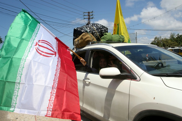 Une femme déplacée tient un drapeau iranien à la fenêtre d'une voiture, alors qu'elle traverse la région d'al-Qasmiyeh, dans le sud du Liban, sur le chemin du retour vers son village natal, le 15 juin 2026 