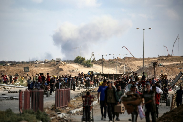 Une colonne de fumée s'élève en
arrière-plan après une frappe alors que des Palestiniens reviennent d'un point de distribution alimentaire dans le centre de la bande de Gaza, le 5 octobre 2025