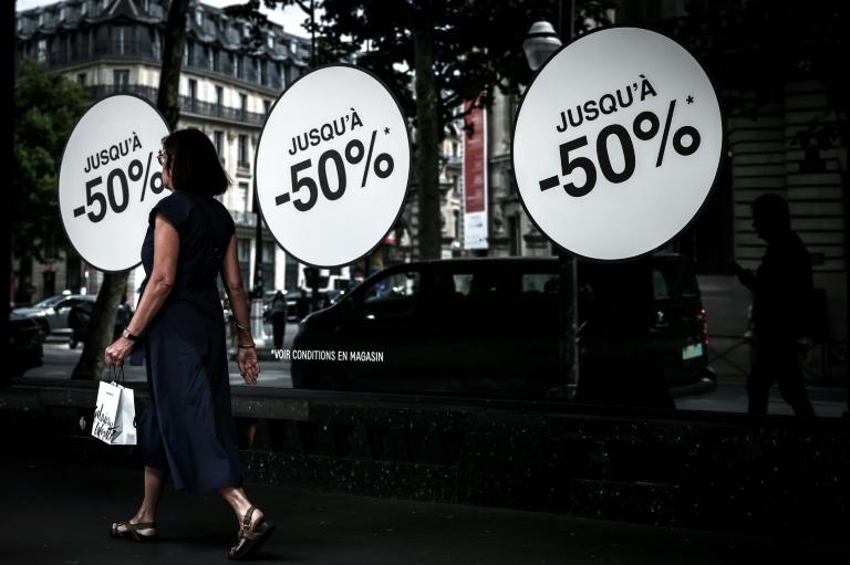 Une passante marche à côté d'une vitrine annonçant les soldes, le 25 juin 2025 à Paris