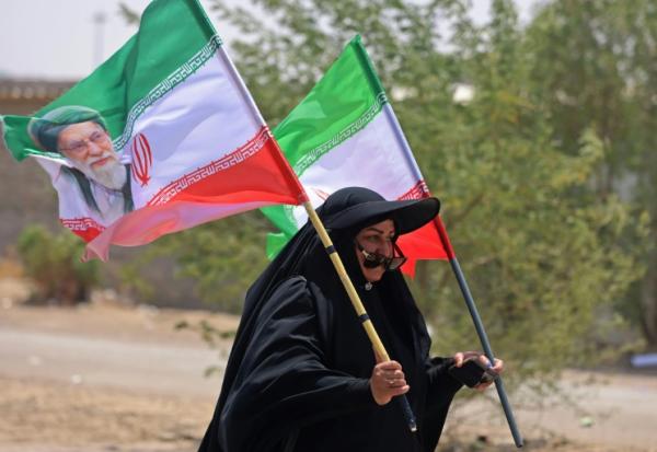 Une pèlerine iranienne brandit des drapeaux iraniens dont l'un comprend un portrait du guide suprême Ali Khamenei, tué dans un bombardement américain, le 29 juillet 2026 dans la ville-frontière de Zurbatiyah, en Irak