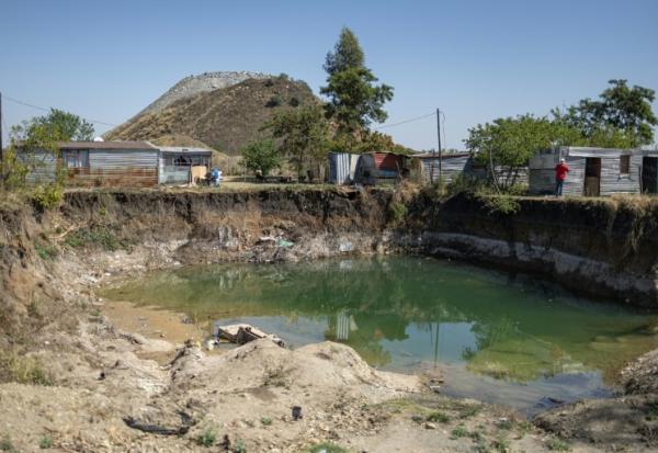 Des habitations surplombent une fosse à ciel ouvert creusée par des mineurs illégaux à la recherche de chrome à Bapong, un village minier de la province du Nord-Ouest (Afrique du Sud), le 25 août 2026