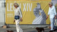 Deux personnes promènent leur chien près d'une affiche annonçant la venue du pape Léon XIV, le 5 juin 2026 à Madrid