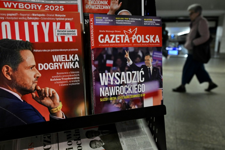 Une femme traverse un passage souterrain devant un kiosque vendant des magazines dont les Unes montrent les candidats à la présidentielle polonaise de 2025, Rafal Trzaskowski (g) et Karol Nawrocki (d), à Varsovie, le 19 mai 2025