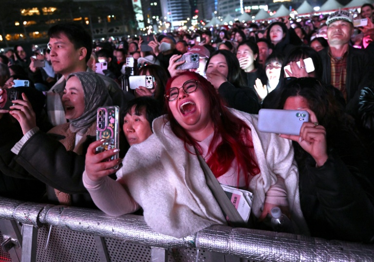 Des fans de BTS assistent au concert de retour du boys band de K-pop devant un écran installé sur le lieu de l'événement à Séoul, le 21 mars 2026