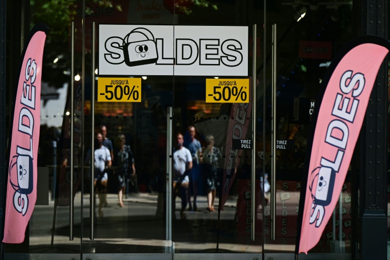 Des passants se tiennent devant la vitrine d'un magasin annonçant des réductions à l'occasion des soldes d'été, à Béziers, dans l'Hérault, le 28 juin 2025