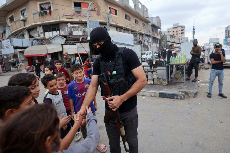 Un membre des forces de sécurité intérieure loyales au groupe palestinien Hamas salue de s enfants dans le camp de réfugiés de Nousseirat, dans le centre de la bande de Gaza, le 12 octobre 2025