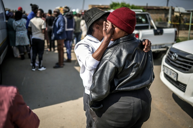 Un résident réconforte une autre personne près du lieu où des hommes armés de fusils d’assaut ont tué 17 personnnes dans un bar à Johannesburg le 27 septembre 2026