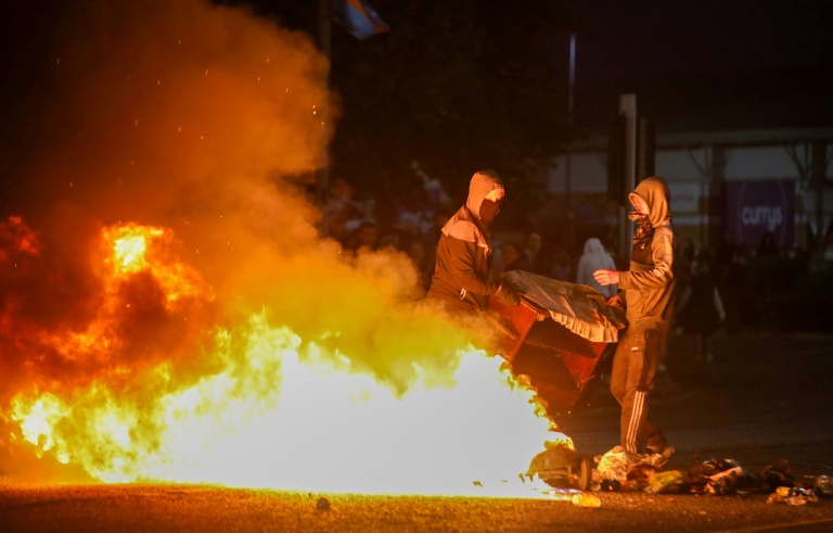 Des manifestants masqués alimentent un feu sur une route lors d'une troisième nuit d'émeutes visant des immigrés à Ballymena, en Irlande du Nord, le 11 juin 2025