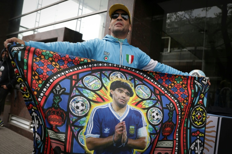 Un supporter tient un drapeau à l'effigie de Diego Maradona, avant une audience du procès sur le décès de la légende du football argentin, devant le tribunal à San Isidro, le 8 octobre 2026 en Argentine