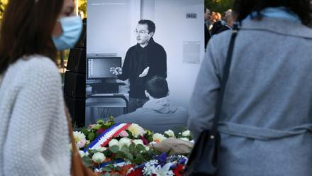 Des personnes passent devant une photographie de Samuel Paty lors d'une cérémonie hommage organisée à Eragny-sur-Oise, au nord-ouest de Paris, le 16 octobre 2021