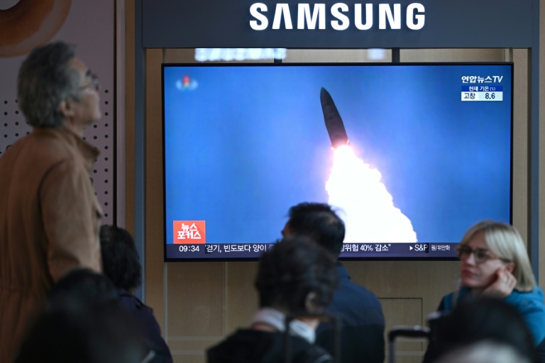 Des personnes sont assises devant un écran de télévision diffusant un journal télévisé avec des images d'archives d'un test de missile nord-coréen, dans une gare de Séoul, le 22 octobre 2025